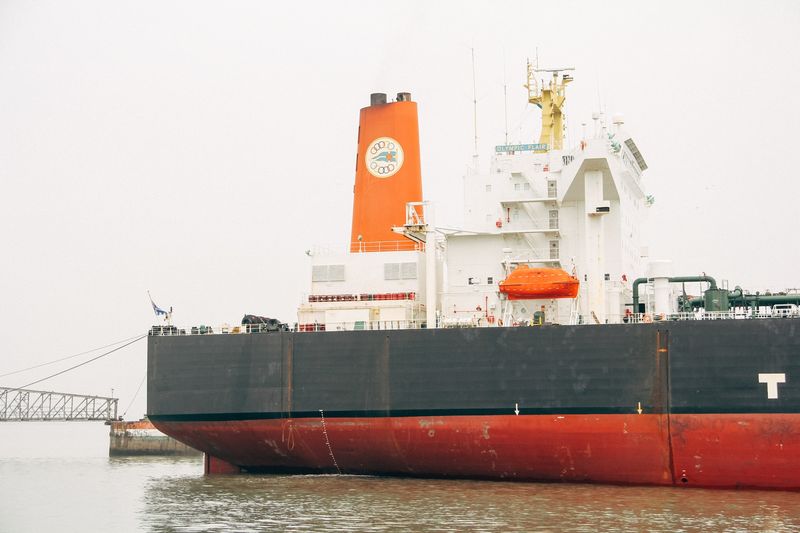 Huge tanker hull, orange funnel with Olympic rings, grey sky