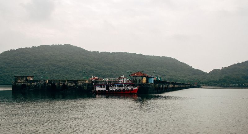 Red ferry at a long grey jetty, misty green hills