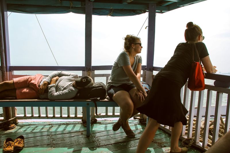 Three travelers on a ferry: asleep, sitting, leaning; shoes in front